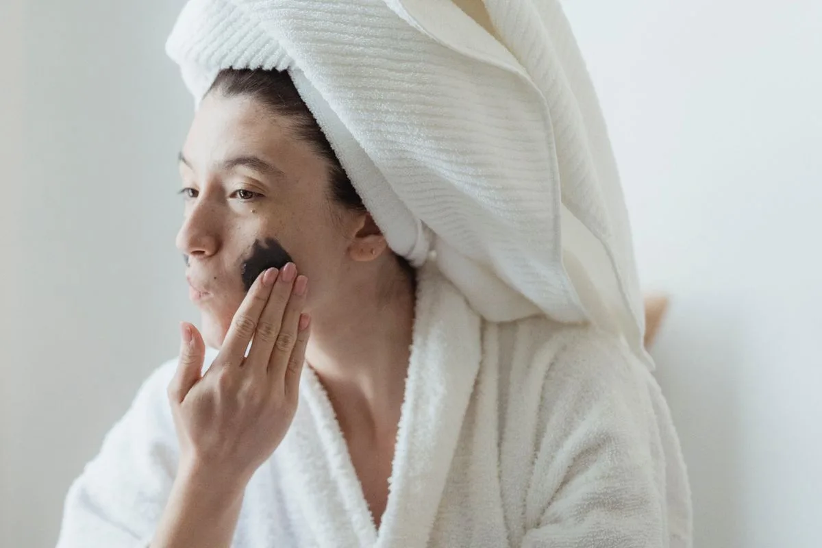 Mujer aplicándose un producto facial con una toalla en la cabeza